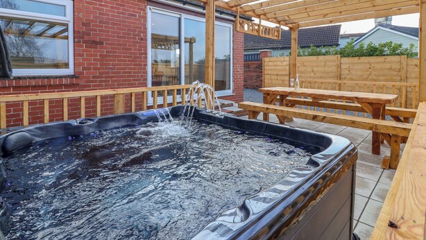 Un bain à remous sous une pergola en bois, avec un mur en briques et des fenêtres en arrière-plan.