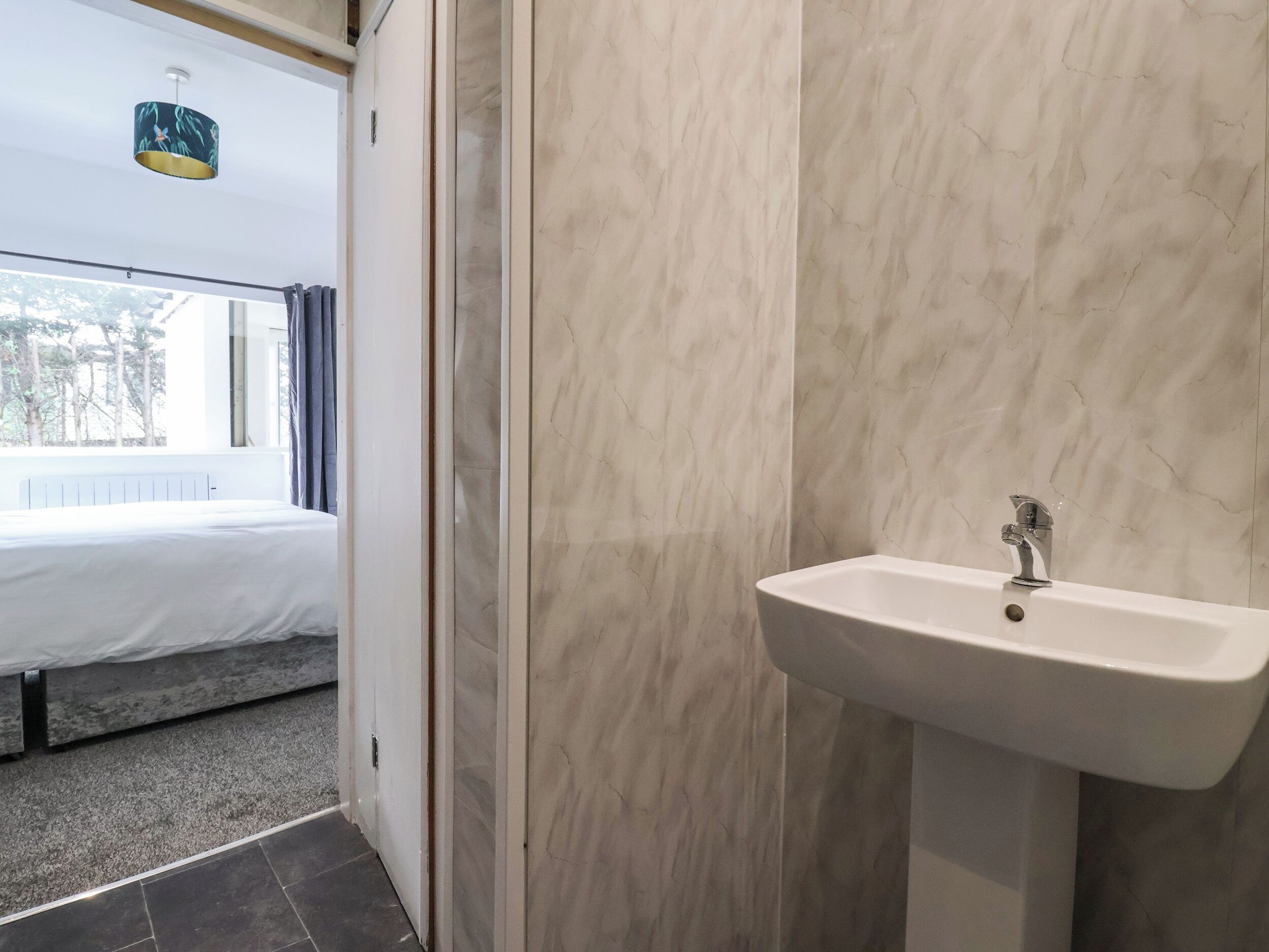 Un baño moderno con pared de mármol, un lavamanos blanco y una ventana con cortinas.