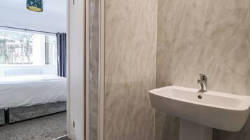 Un baño moderno con pared de mármol, un lavamanos blanco y una ventana con cortinas.
