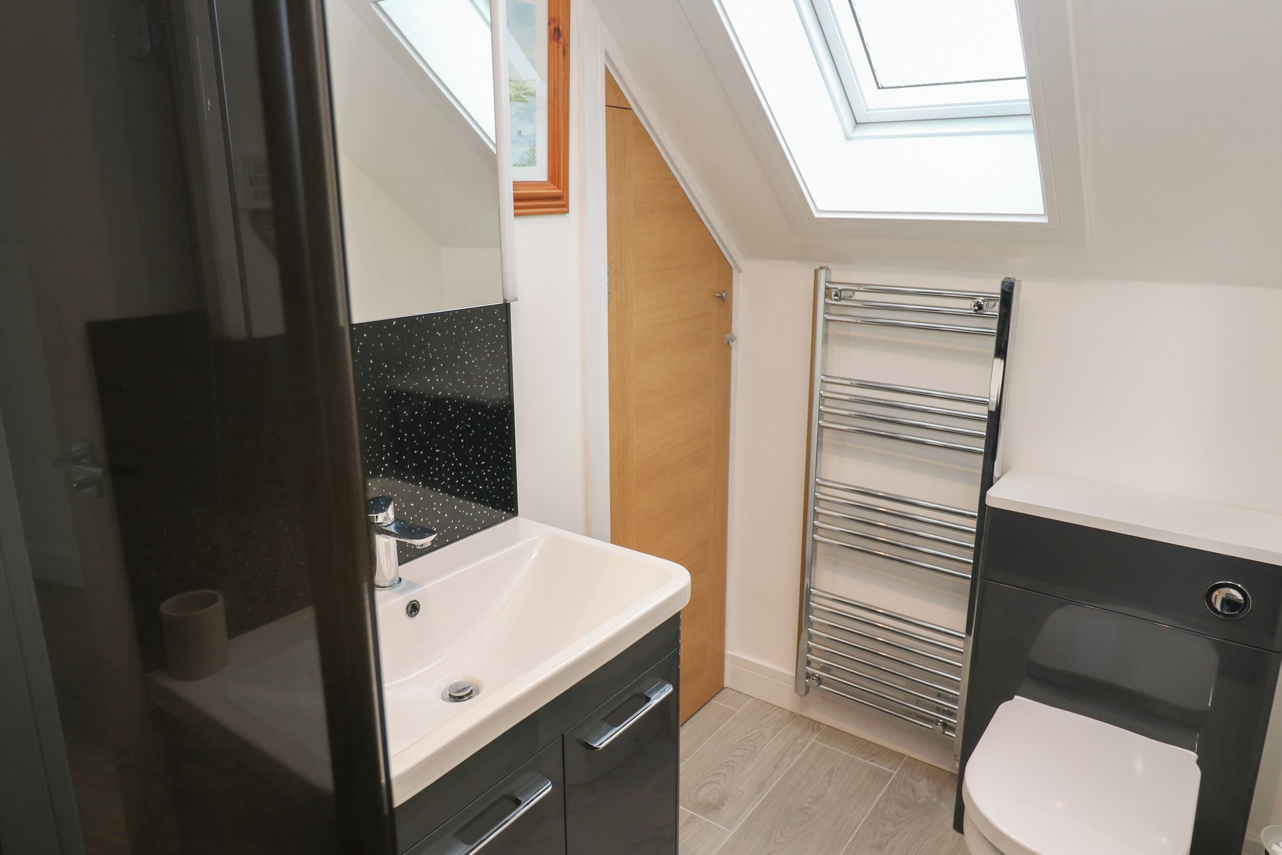 Een moderne badkamer met dakraam, een witte wastafel, een zwart kastje en een toilet.