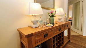 Een houten console tafel met twee lampen, een vaas met bloemen en een fles champagne.