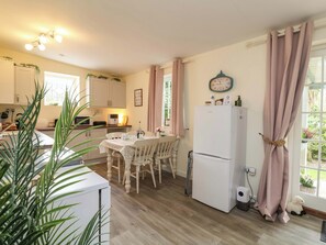 A kitchen with a dining table, chairs, a refrigerator, and a clock on the wall. - Sunset Cottage (Barnstaple)