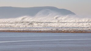 A beach with waves crashing onto the shore and a distant mountain. - Sunset Cottage (Barnstaple)