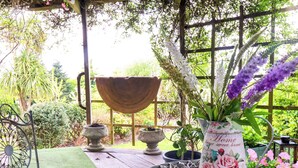 A garden patio with a metal table, a decorative metal chair, a large planter, and a floral vase. - Sunset Cottage (Barnstaple)