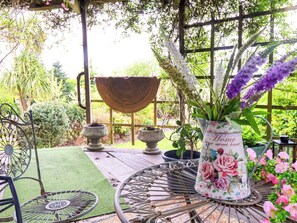 Eine Garten-Terrasse mit einem Metalltisch, einem dekorativen Metallstuhl, einem großen Pflanzgefäß und einer Blumenvase.