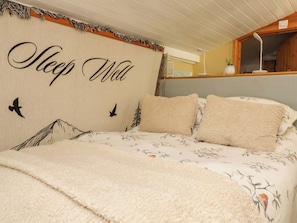 A bedroom with a bed, a wall with 'Sleep Well' text, and a window with a plant. - Sunset Cottage (Barnstaple)
