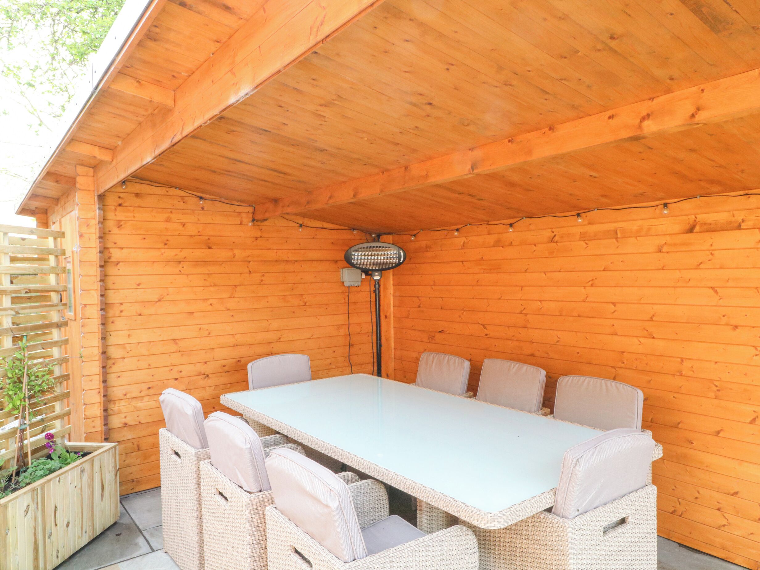 Ett takförsett utomhusområde med ett bord och stolar, en fläkt och ett trästaket.