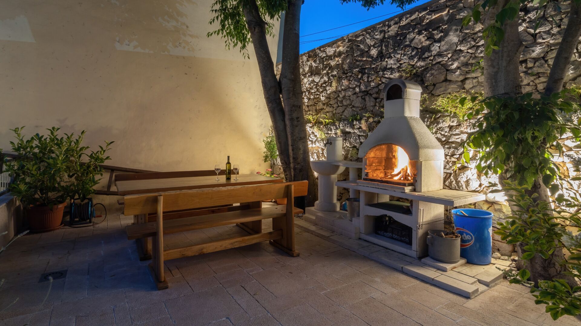 An outdoor seating area with a stone wall, a wooden bench, and a wood-fired oven.