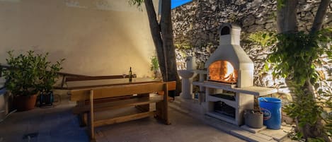 An outdoor seating area with a stone wall, a wooden bench, and a wood-fired oven.
