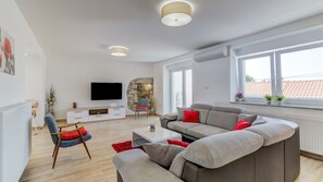 Un salon moderne avec un canapé d’angle, un téléviseur à écran plat, un mur décoratif en pierre et une grande fenêtre offrant une belle vue.