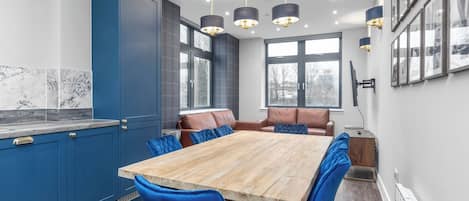 A modern kitchen with a large wooden table, blue chairs, and pendant lights.