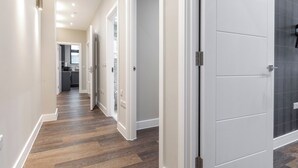 A hallway with wooden flooring, white doors, and recessed ceiling lights.