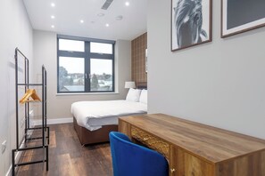 Ein Hotelzimmer mit Bett, Schreibtisch, Stuhl, Kleiderschrank, Fenster mit Stadtblick und Kleiderhaken mit Bügeln.