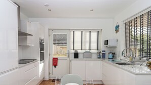 Een compacte keuken met witte kastjes, een magnetron en een broodrooster. Er staat een eettafel gedekt met borden, glazen en bestek. Een branddeken is aan de deur bevestigd.