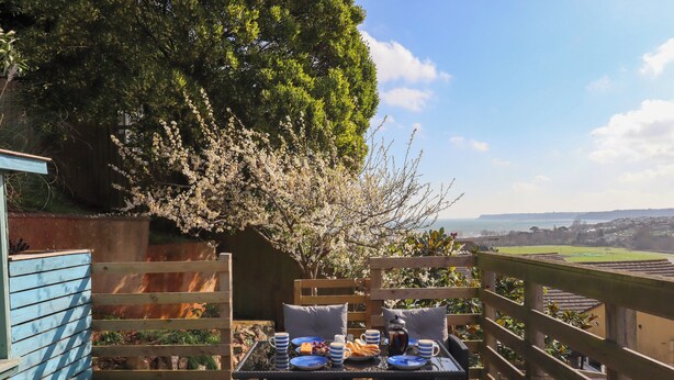 Een houten terras met een ontbijttafel, met uitzicht op een schilderachtig kustlandschap.