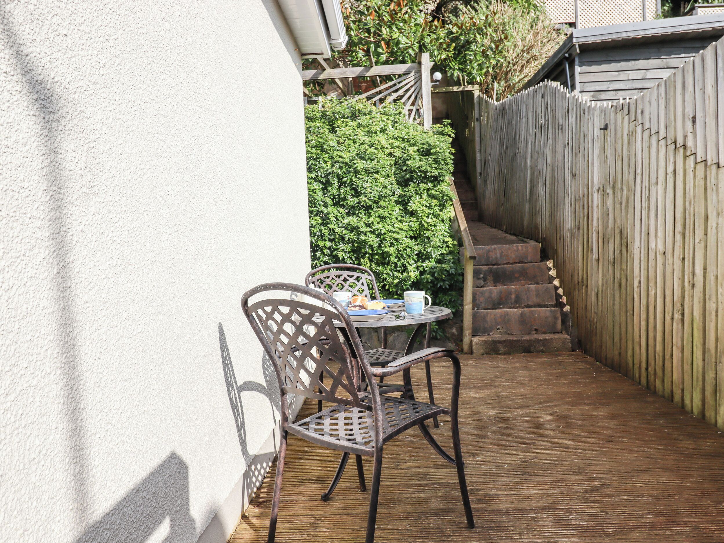 Un patio con mesa y sillas, una terraza de madera, una valla de madera y una escalera que sube a un nivel superior.