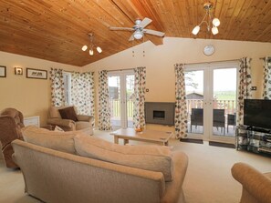 A cozy living room with a fireplace, a television, and a ceiling fan. - Lodge 16 (Torpoint)