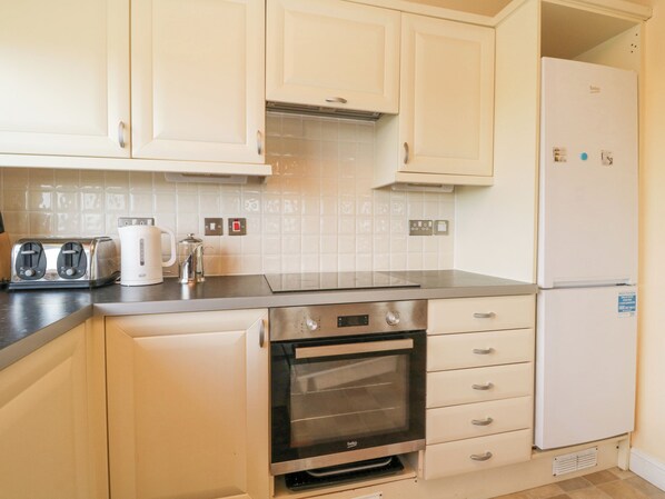 A kitchen with white cabinets, a built-in oven, a refrigerator, and a coffee maker on the countertop. - Lodge 16 (Torpoint)