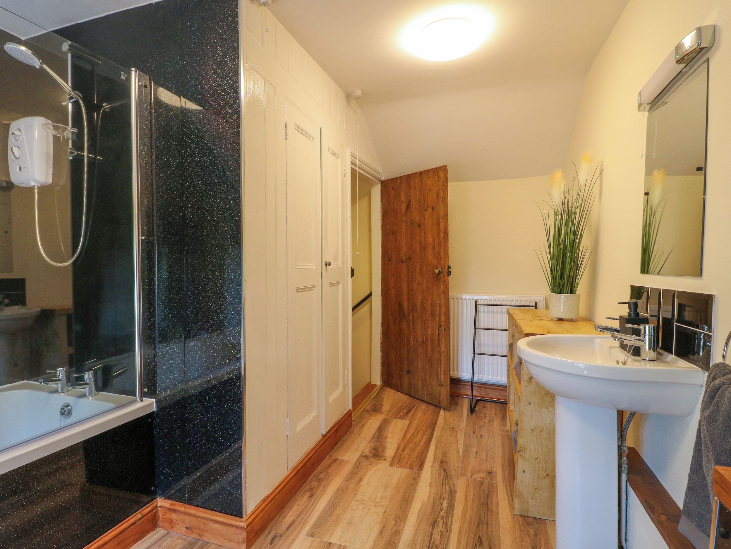 Un bagno con cabina doccia in vetro, lavandino bianco e porta in legno.