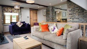 A cozy living room with a grey sofa, wooden coffee table, and a stone fireplace. - The Cosy Peacock (Windermere)
