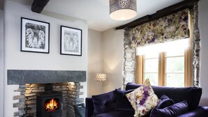 A cozy living room with a stone fireplace, a dark blue sofa, and two framed pictures on the wall. - The Cosy Peacock (Windermere)