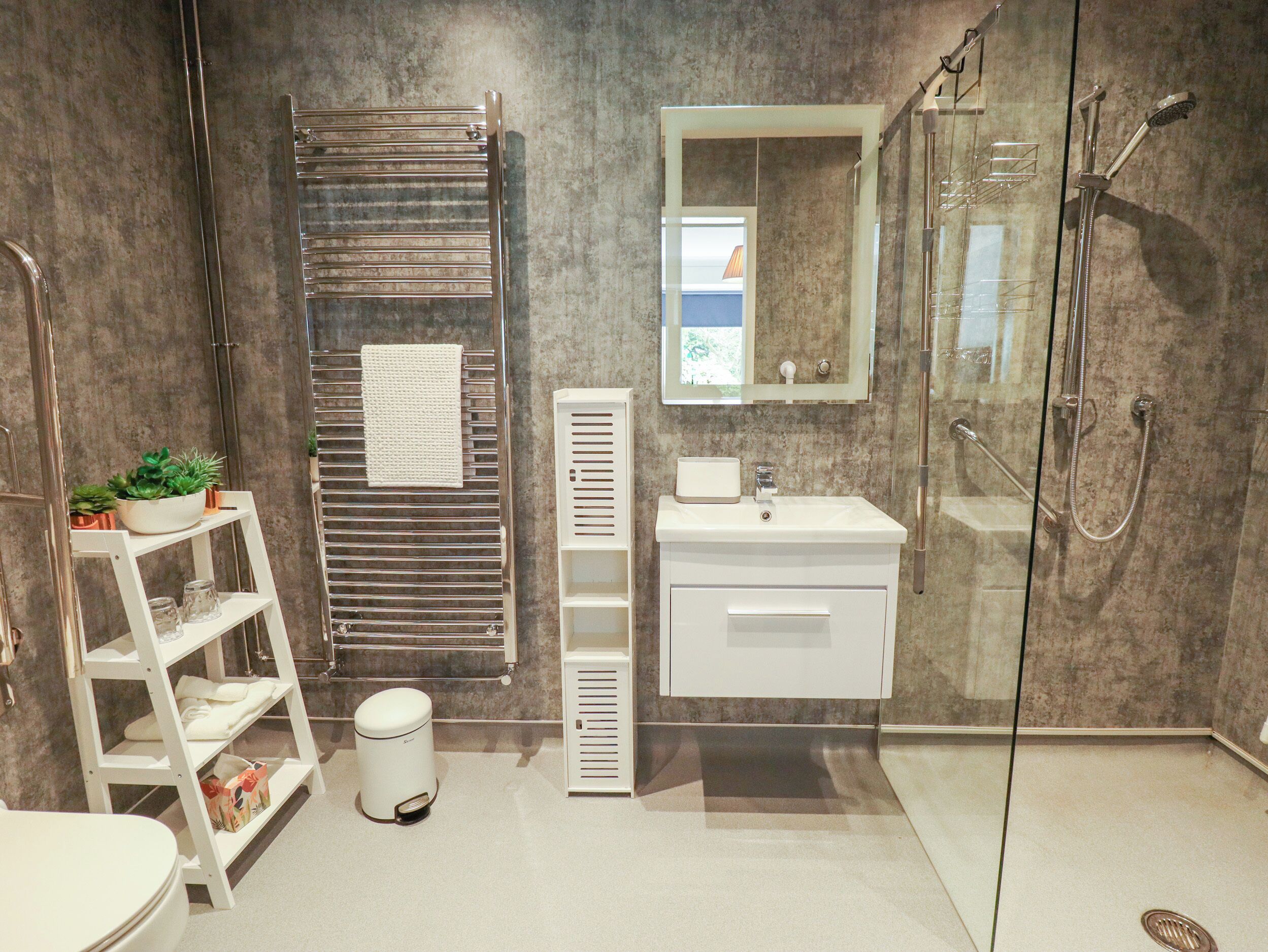 A modern bathroom with a glass shower enclosure, a white sink, and a towel rack with a towel.