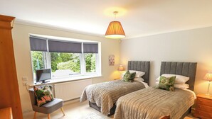 A bedroom with two beds, a desk, a chair, a window with a view, and a lamp. - Number 16 (Woodhall Spa)