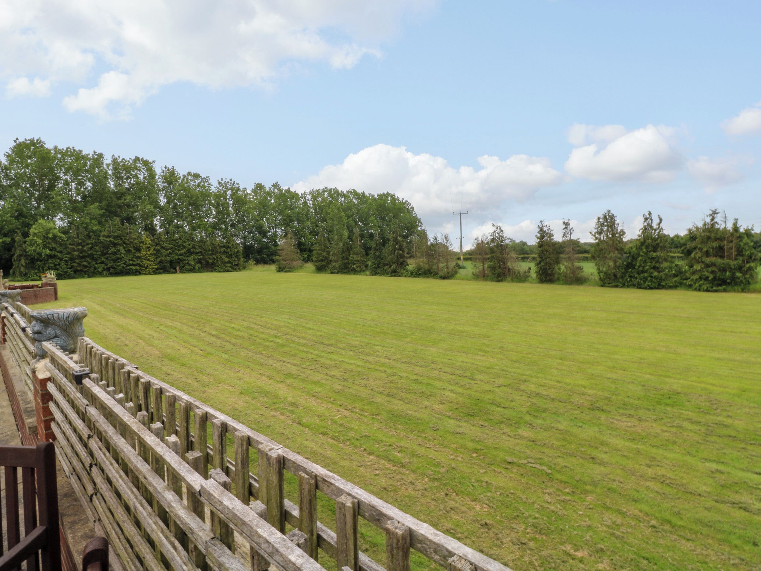 A large, open grassy field with a wooden fence and a stone balustrade.