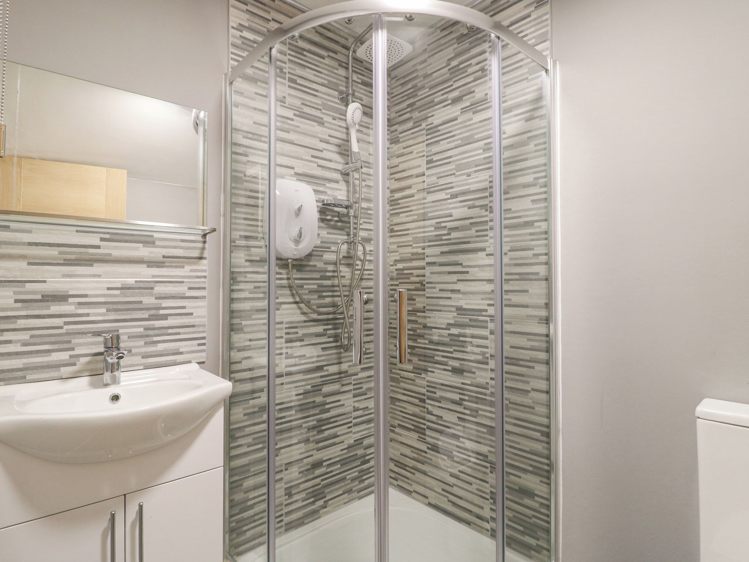 Un baño moderno con ducha envuelta en vidrio, un lavabo blanco y un salpicadero de azulejos.