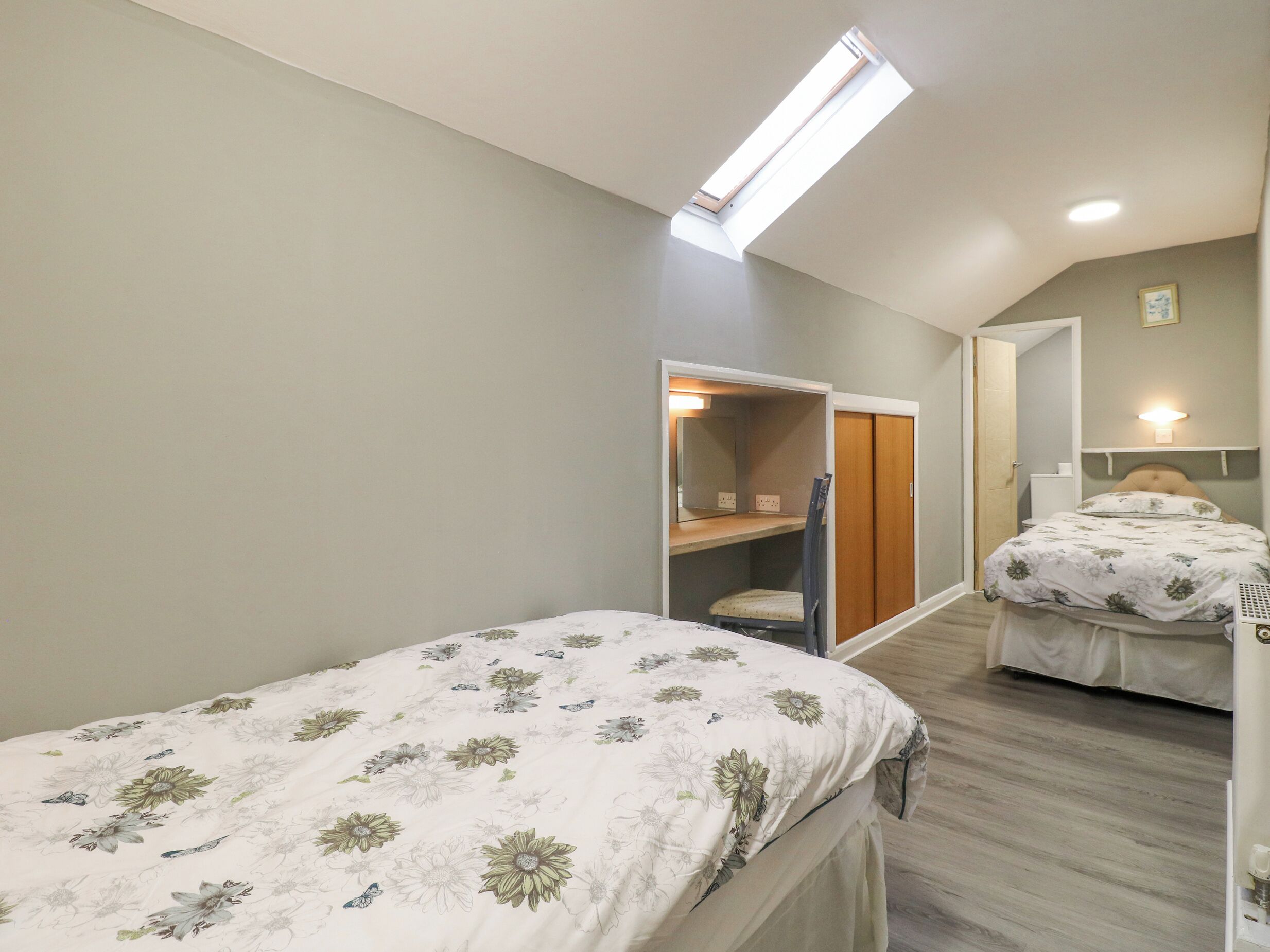 Ein Schlafzimmer mit zwei Betten, einem Oberlicht, einem Kleiderschrank und einem Spiegel.