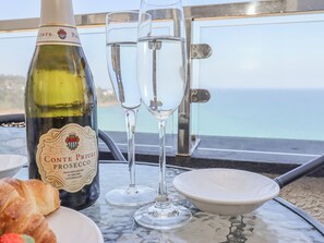 Une bouteille de Prosecco Conte Priuli, deux verres, un saladier et un croissant sur une table donnant sur la mer.