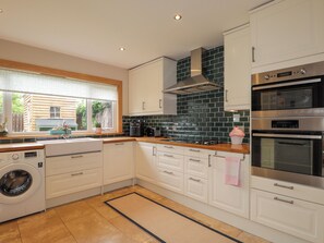 A modern kitchen with white cabinets, a built-in oven, a microwave, and a washing machine. - Garry Isle (Inverness)