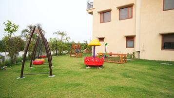 A grassy outdoor area with playground equipment including swings, a slide, and a climbing structure.