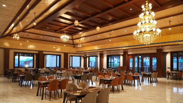 Un comedor amplio con varias mesas y sillas, ventanas grandes y candelabros.