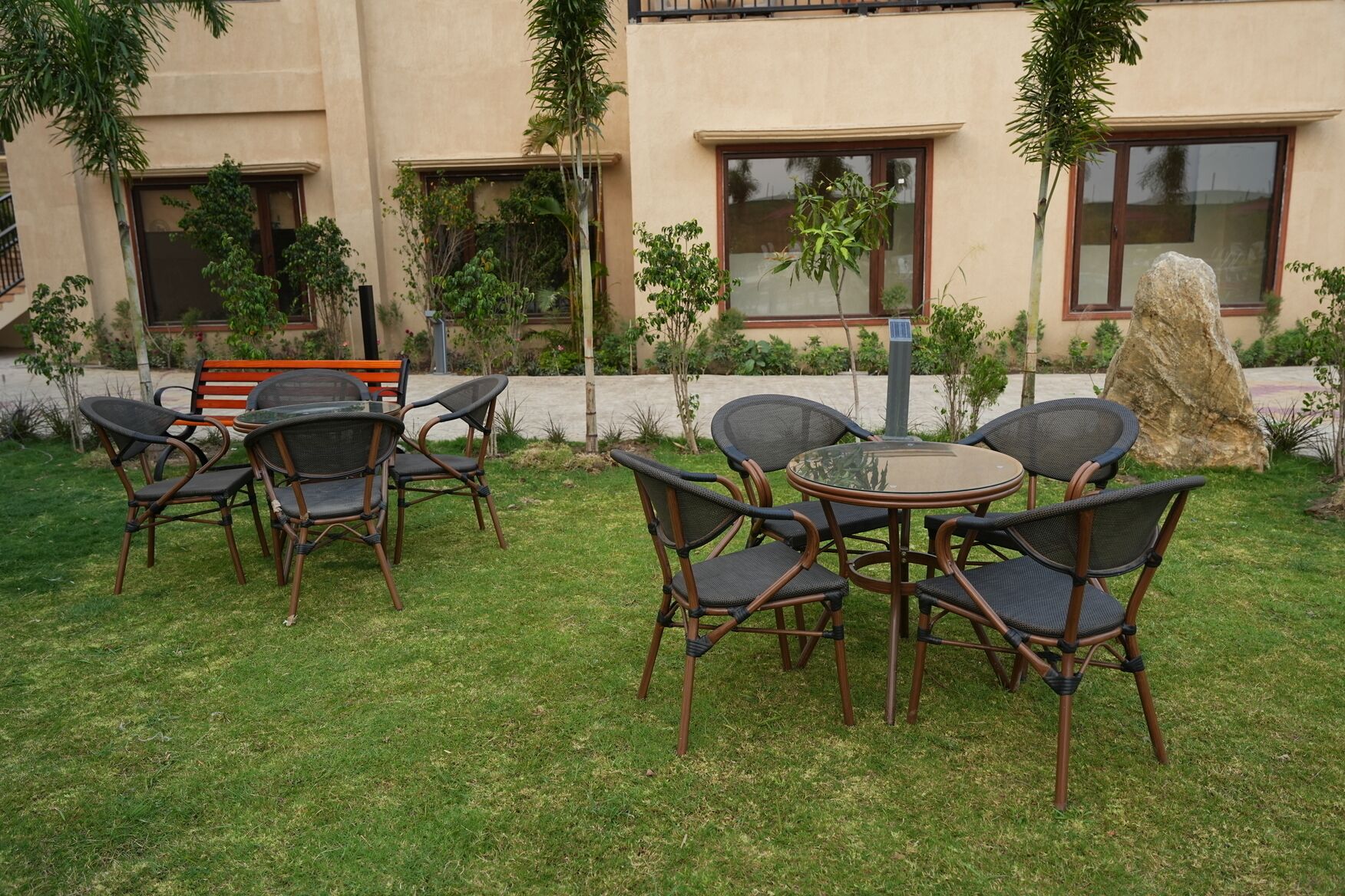 An outdoor seating area with wicker chairs and a glass table, surrounded by a well-maintained lawn and a building with large windows.