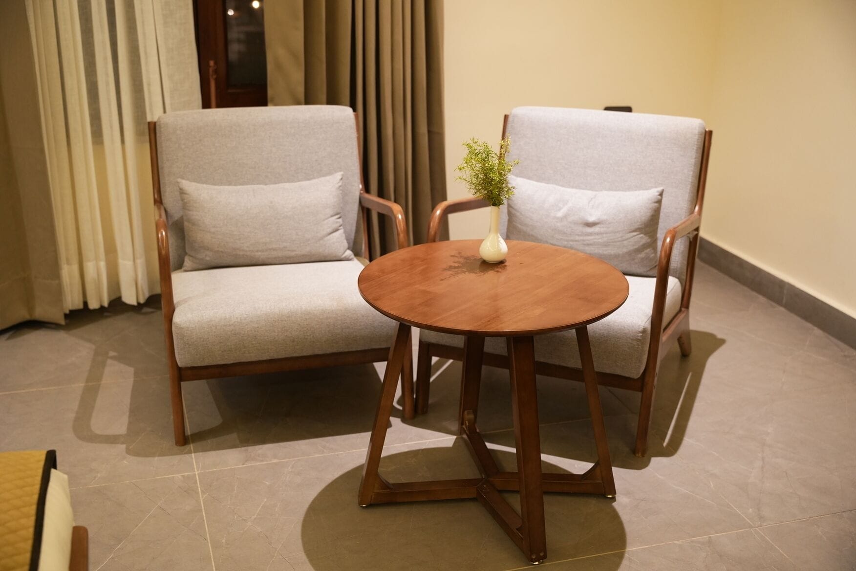 Ein Zimmer mit zwei grauen Polstersesseln und einem runden Holztisch mit einer kleinen weißen Vase.