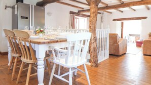 A dining area with a wooden table set for four, surrounded by white chairs. A white railing separates the dining area from the living space. - Skiber Coombe (Callington)