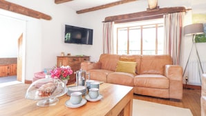 A cozy living room with a wooden table, a leather sofa, and a television mounted on the wall. - Skiber Coombe (Callington)