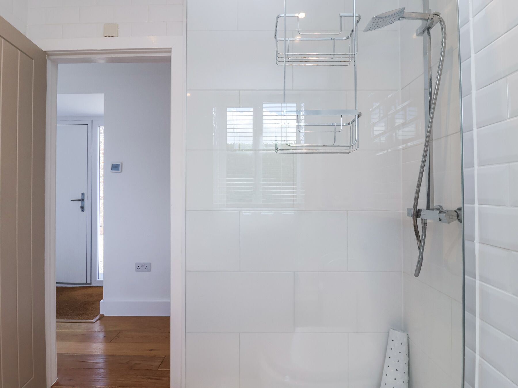 Un baño moderno con cabina de ducha de vidrio, paredes de azulejos blancos y suelo de madera.