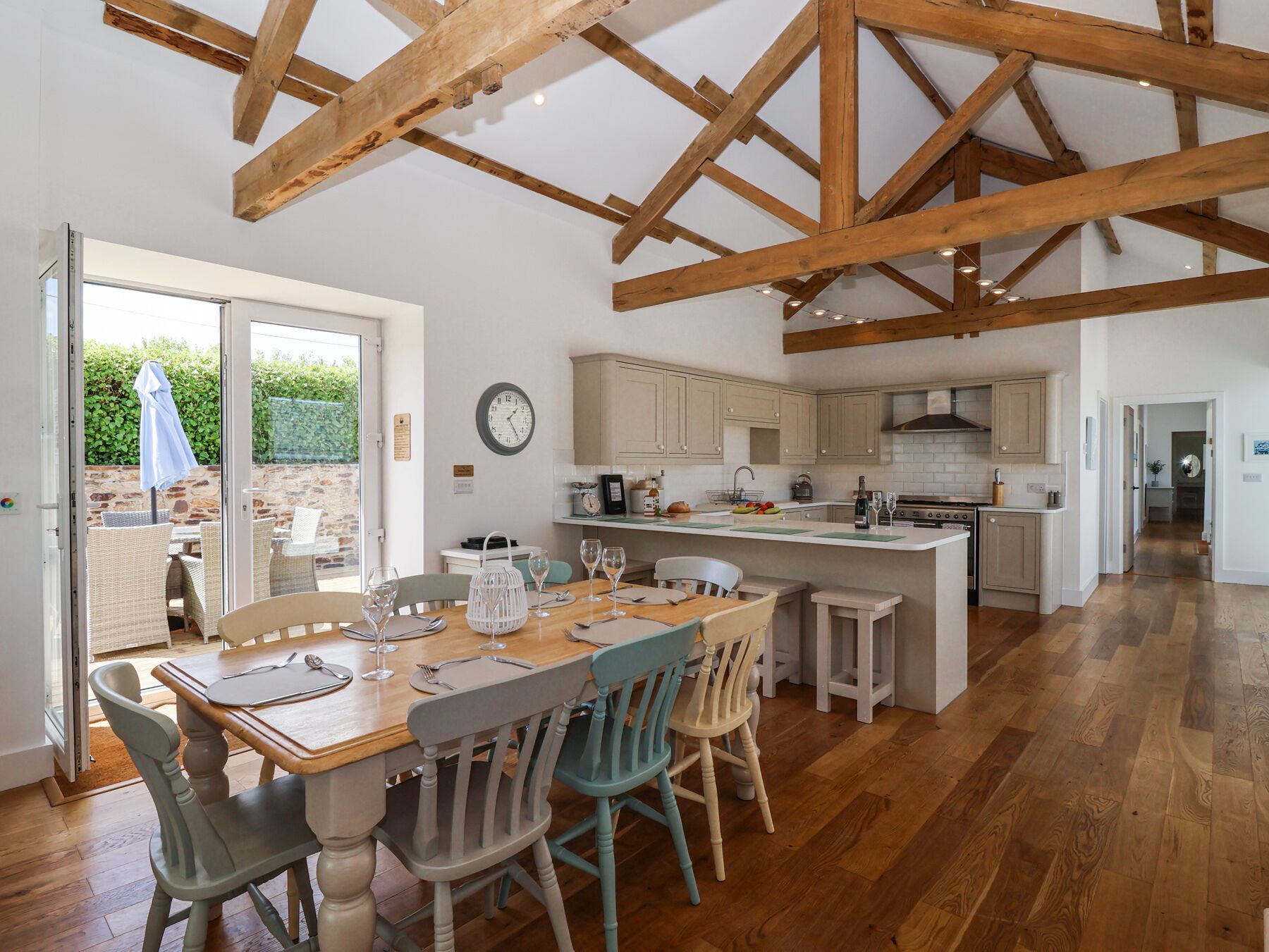 A spacious kitchen with wooden beams, a dining area with a table set for four, and a view of the outdoors.