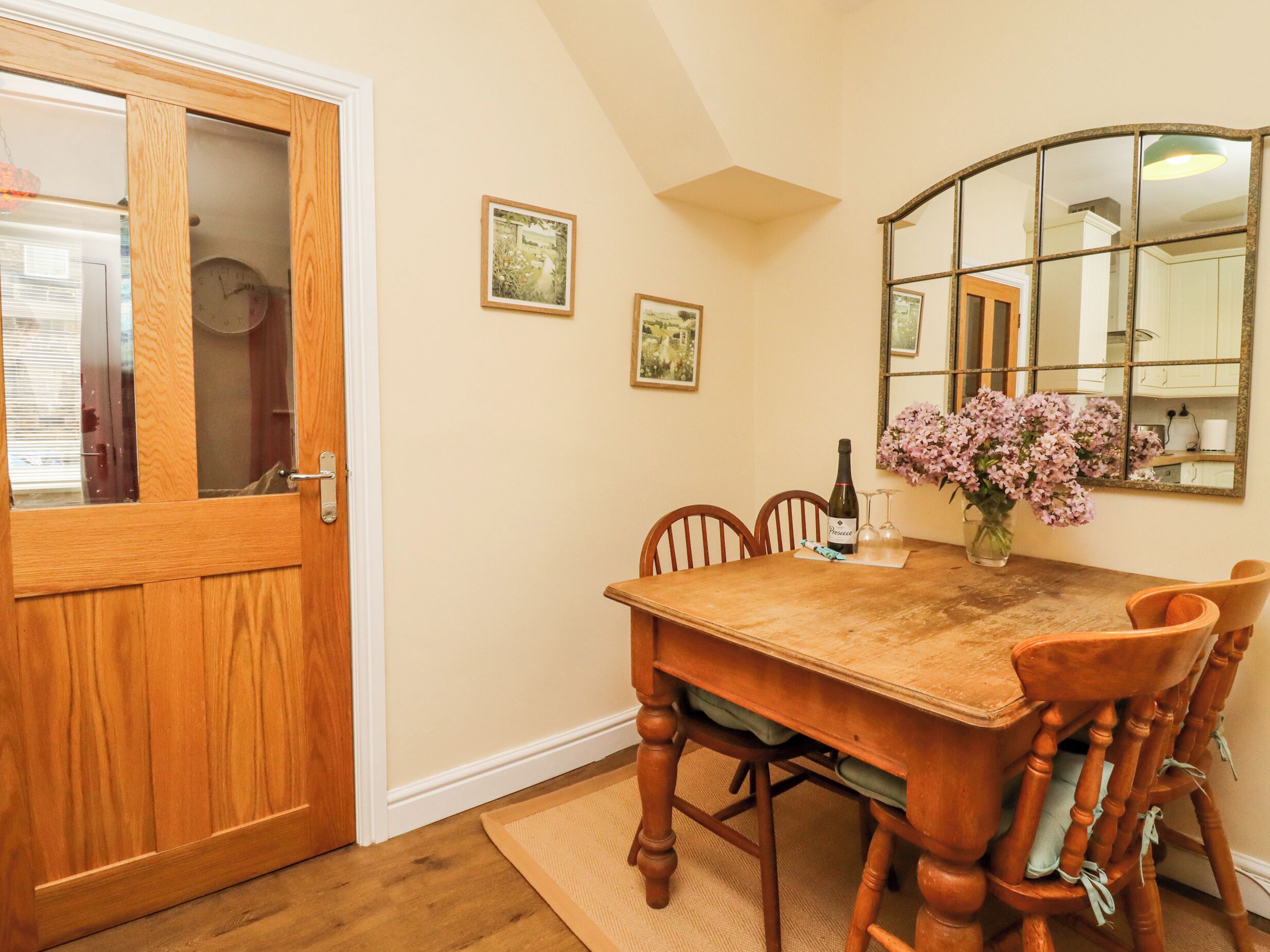 A dining room with a wooden table, chairs, a vase with flowers, and a clock on the wall.