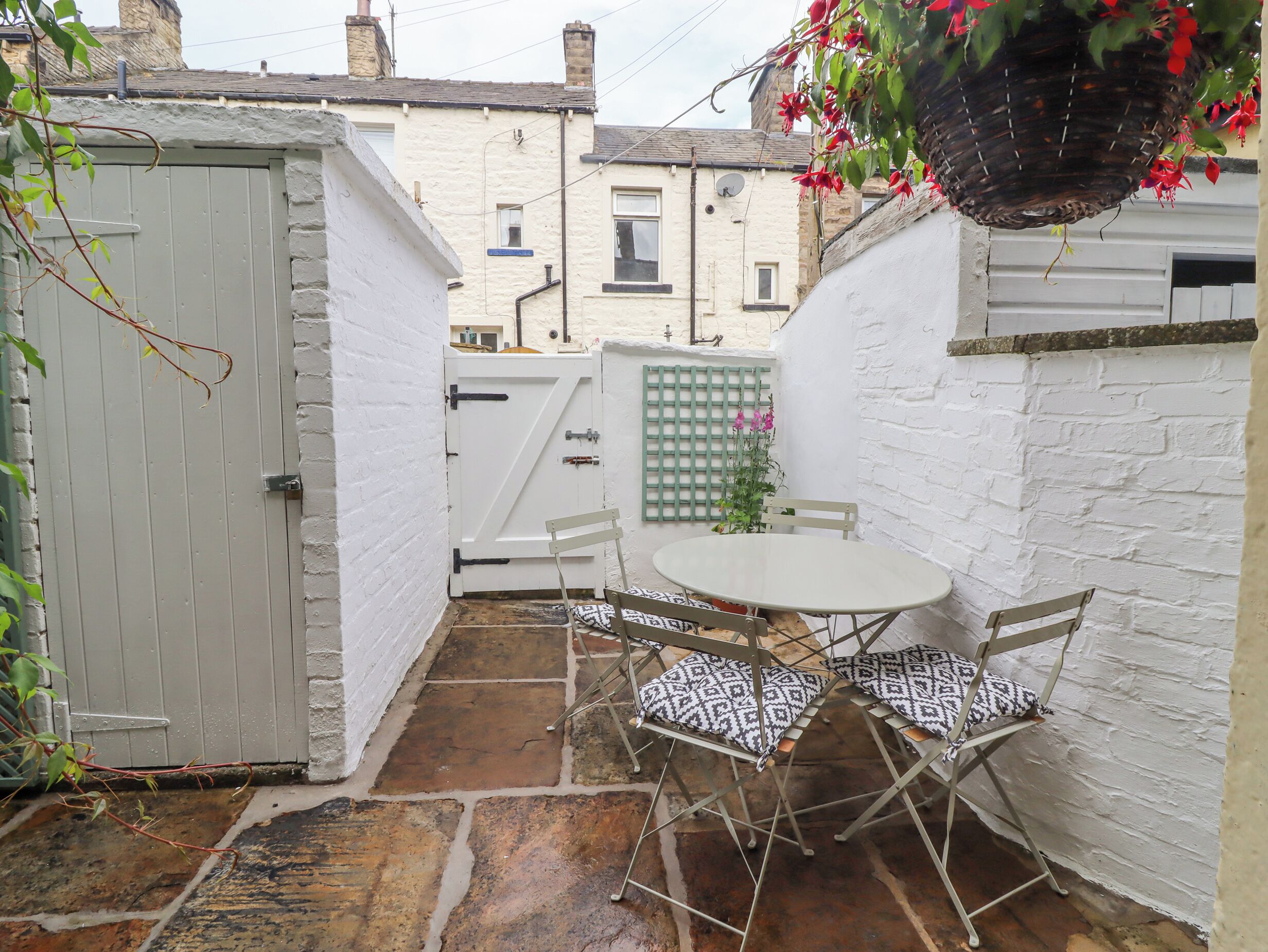 A small patio with a white table and two chairs, a white door, and a green gate.