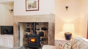 A living room with a stone fireplace, a television on a cabinet, and a lamp on a side table. - 4 Pembroke Street (Skipton)