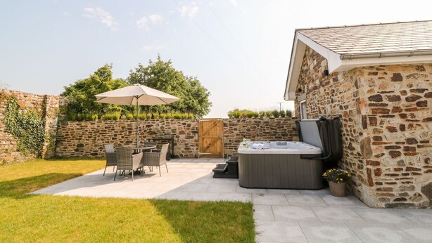 Ein Steinhaus mit einer Terrassenanlage, die einen Tisch, Stühle, eine Whirlwanne und einen Sonnenschirm bietet.