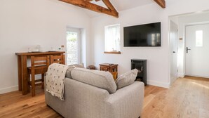 Ein gemütliches Wohnzimmer mit einer Couch, Holzbalken, einem Fernseher, einem Kamin und einem Essbereich mit Tisch und Stühlen.