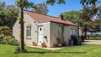 A single-story house with a red-tiled roof, a small porch, and a garden with potted plants.