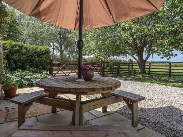 Ein Holztisch für ein Picknick mit einem braunen Sonnenschirm, umgeben von Kies und Topfpflanzen.