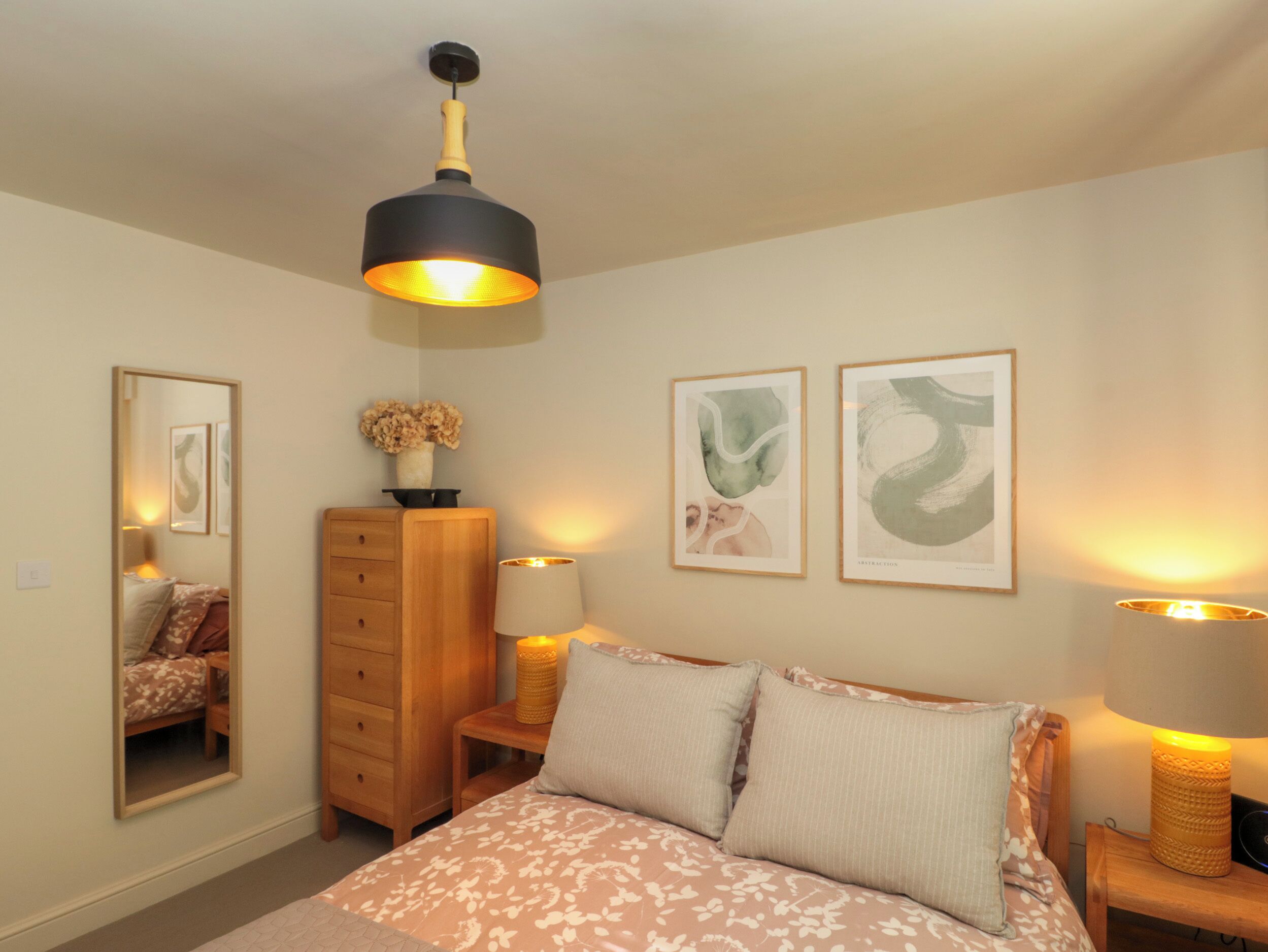 A bedroom with a bed, bedside lamps, a dresser, a mirror, and two framed artworks on the wall.