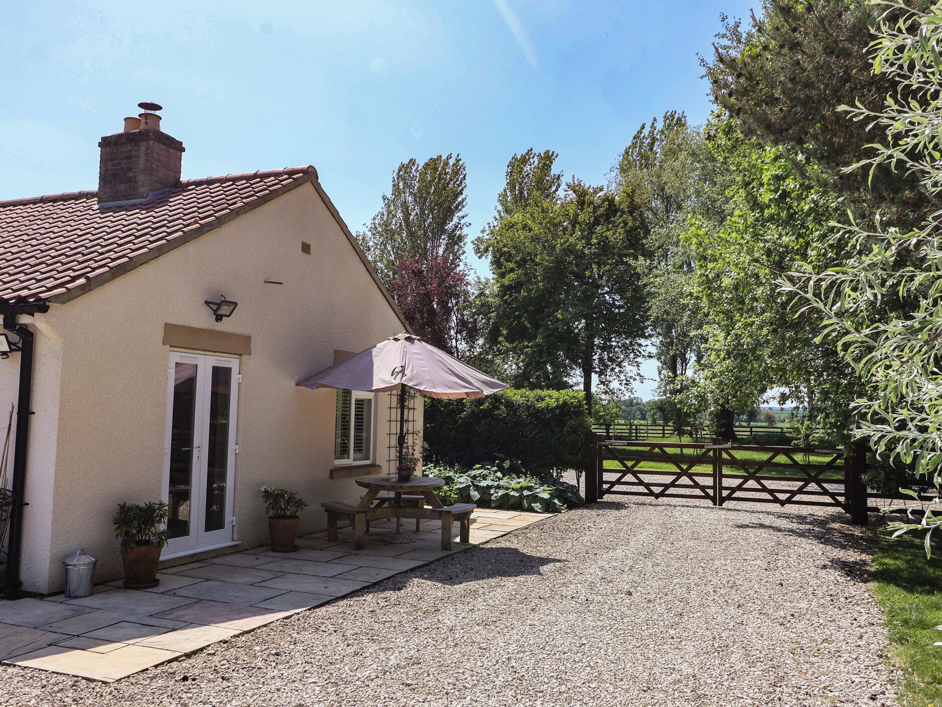 A house with a tiled roof, a door, a window, a patio with a table and chairs, and a gravel driveway.