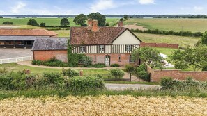 A traditional half-timbered house with a garden and fields in the background.